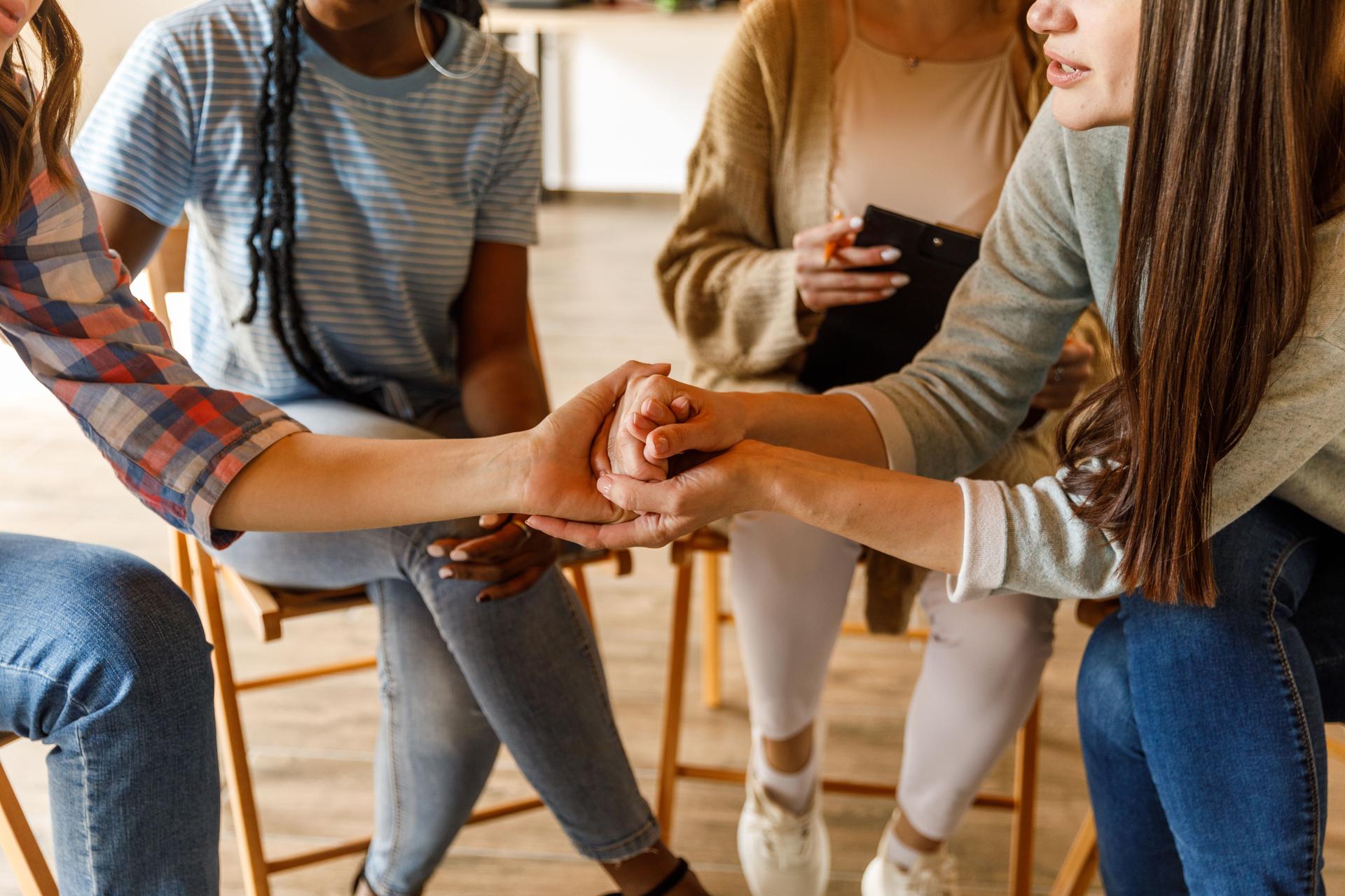 Holding hands with a young woman to show support during a group therapy session